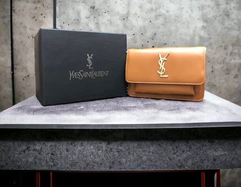A camel YSL (Yves Saint Laurent) leather bag with the brand's logo on the front, displayed next to its packaging.