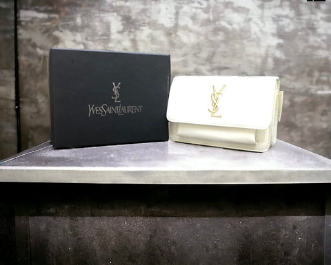 A white YSL (Yves Saint Laurent) leather bag with the brand's logo on the front, displayed next to its packaging.